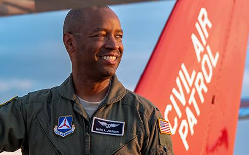 An adult Civil Air Patrol member in a flight suit beside the tail of a CAP aircraft